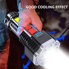 Hand holding a black flashlight with bright beam and red side switch